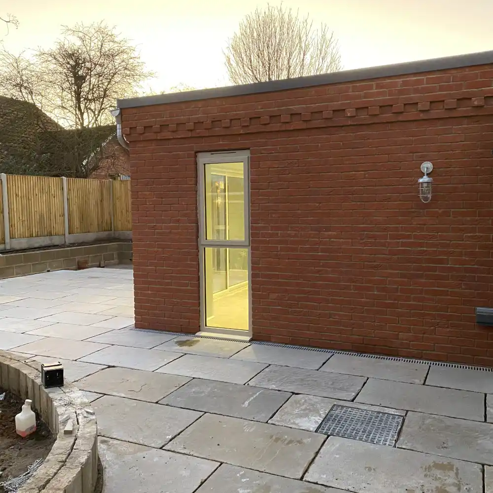 Garage conversion exterior with brickwork, glazed door and paved patio by Image Home Improvements