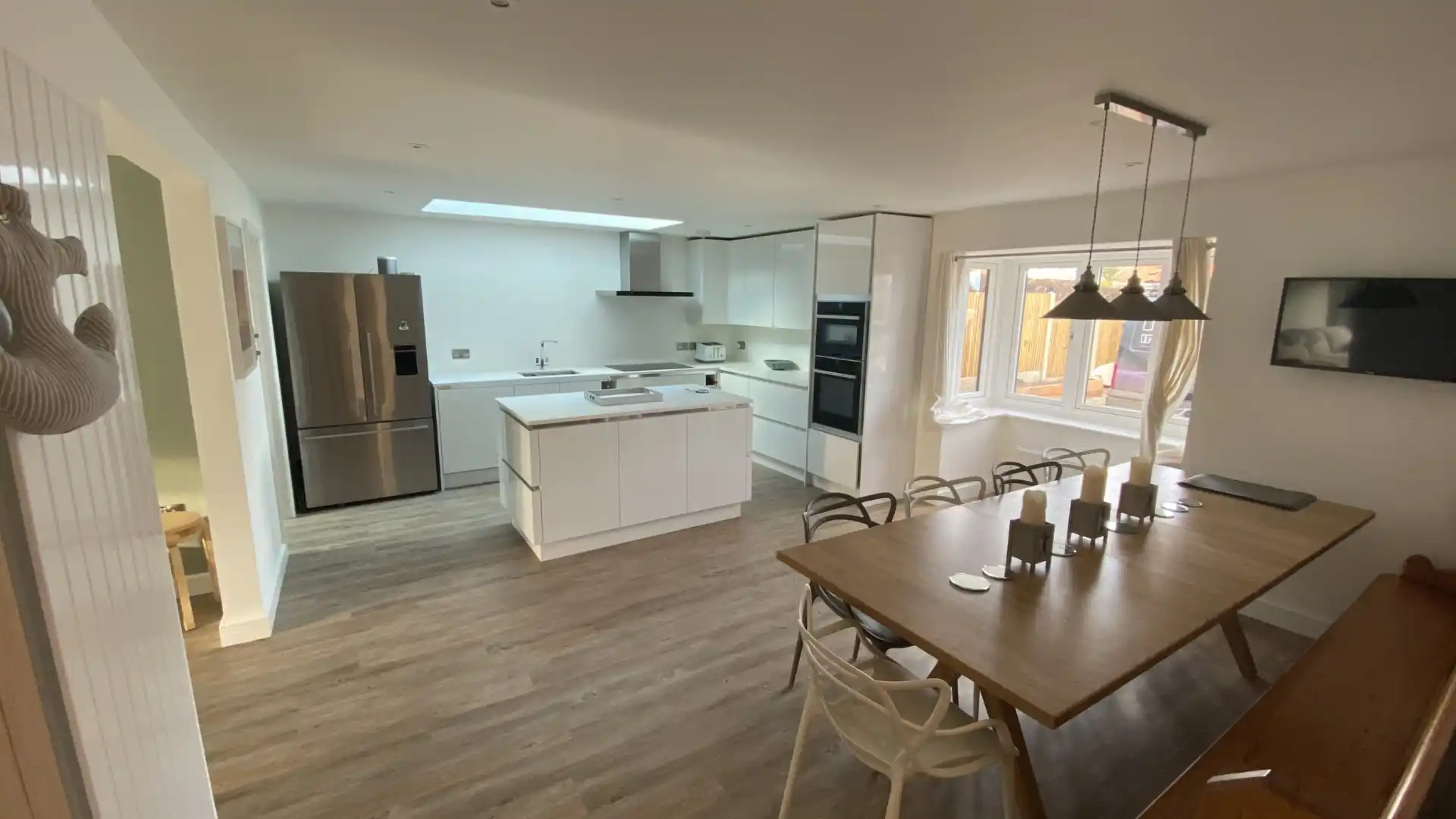 Open plan kitchen and dining renovation with white cabinetry, central island and wood flooring by Image Home Improvements