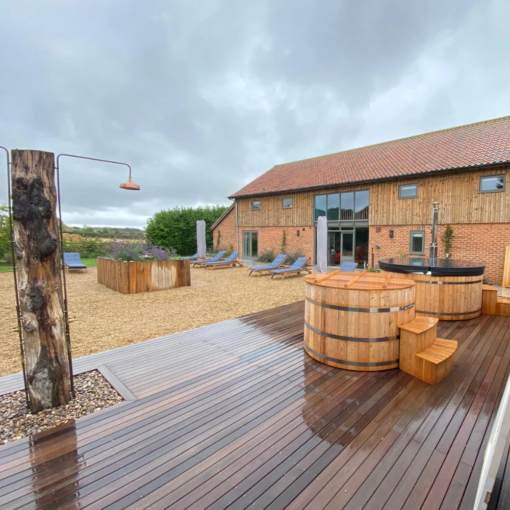 Outdoor timber decking area with wooden hot tubs and converted barn by Image Home Improvements