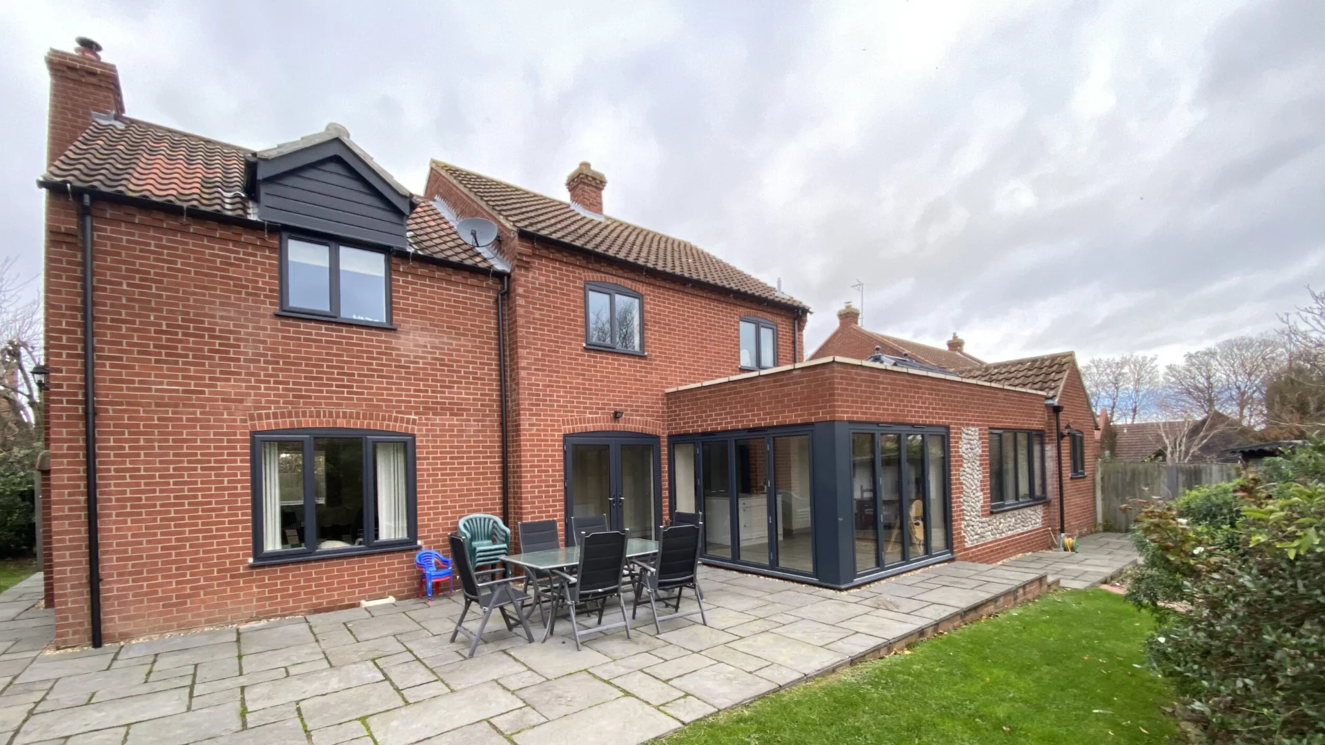 Brick home extension with black framed glass doors opening onto a paved garden patio.