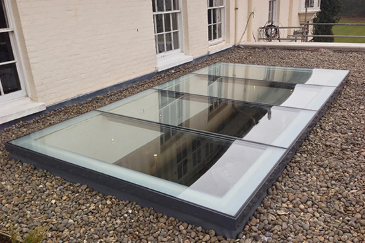 Large flat glass skylight installed on a gravel roof outside a period property.